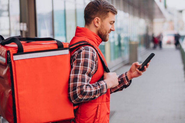 homem usando o celular com mochila ifood nas costas